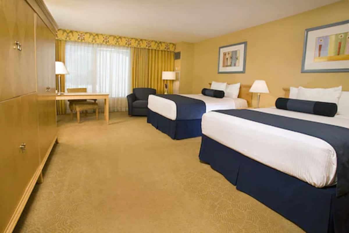 A hotel room with two beds, a desk, and a chair.