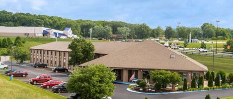 A building with a parking lot, a grassy area, and a road with vehicles.
