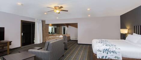 A hotel room with a bed, a sofa, a small table, a ceiling fan, and a bathroom visible through an open door.