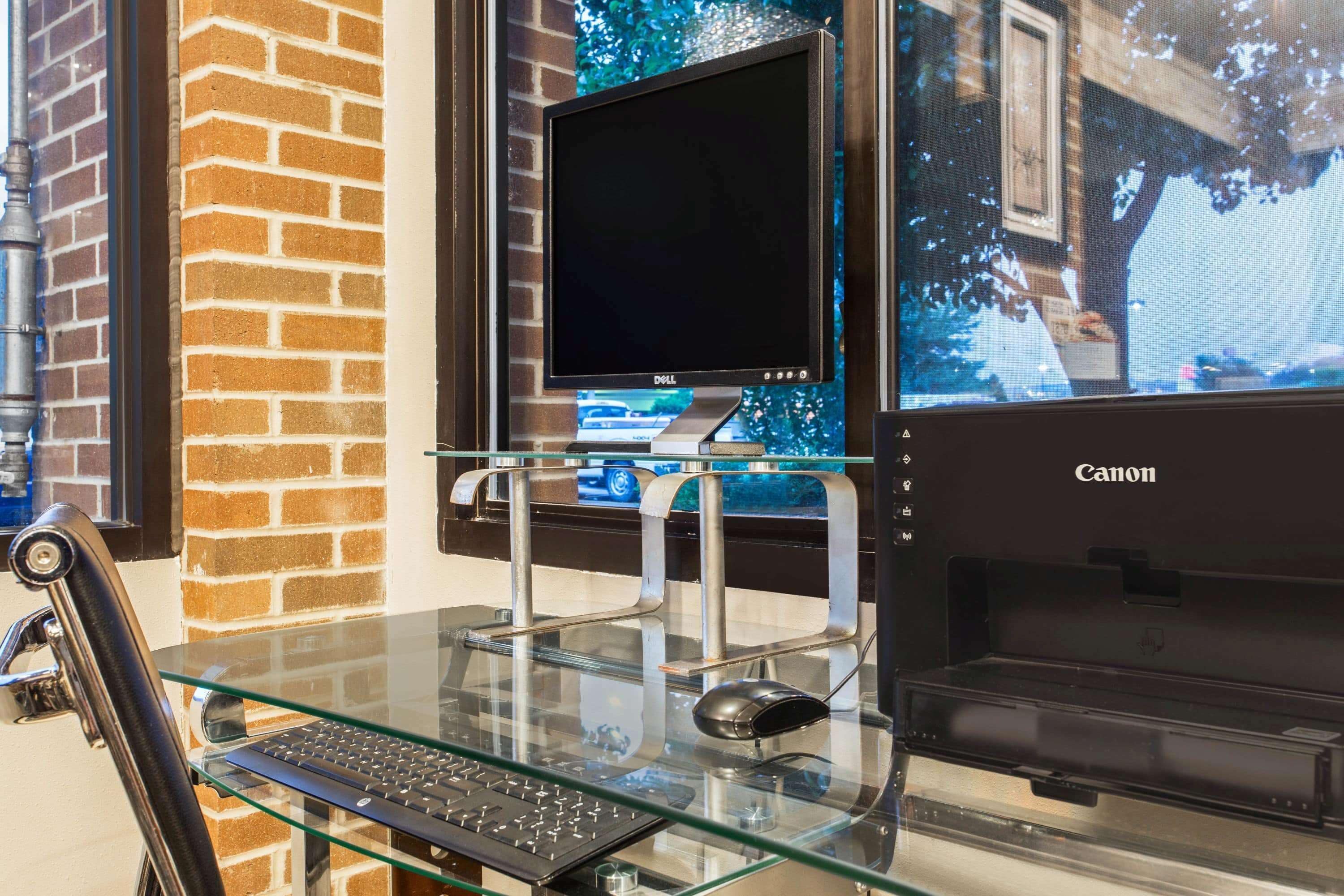 Ein Glastisch mit einem Laptop, einer Maus und einem Canon-Drucker.