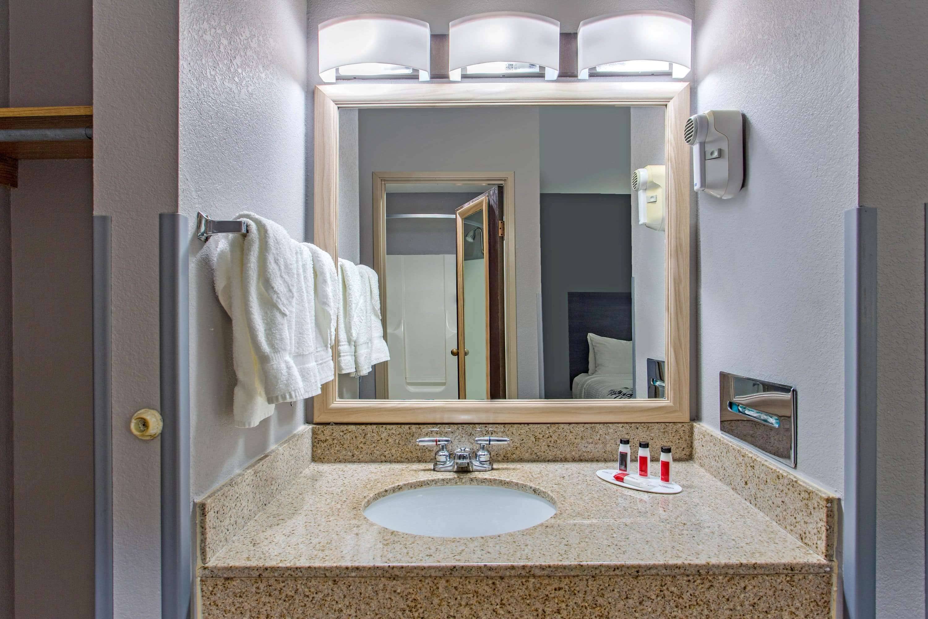 Un baño con encimera de granito, lavamanos, espejo y toallero.
