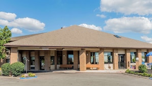 A single-story building with a flat roof, a brick facade, and a sign that reads "Baymont." There are two benches outside, a small garden area, and a parking lot in front. - Baymont by Wyndham Lancaster (Lancaster)
