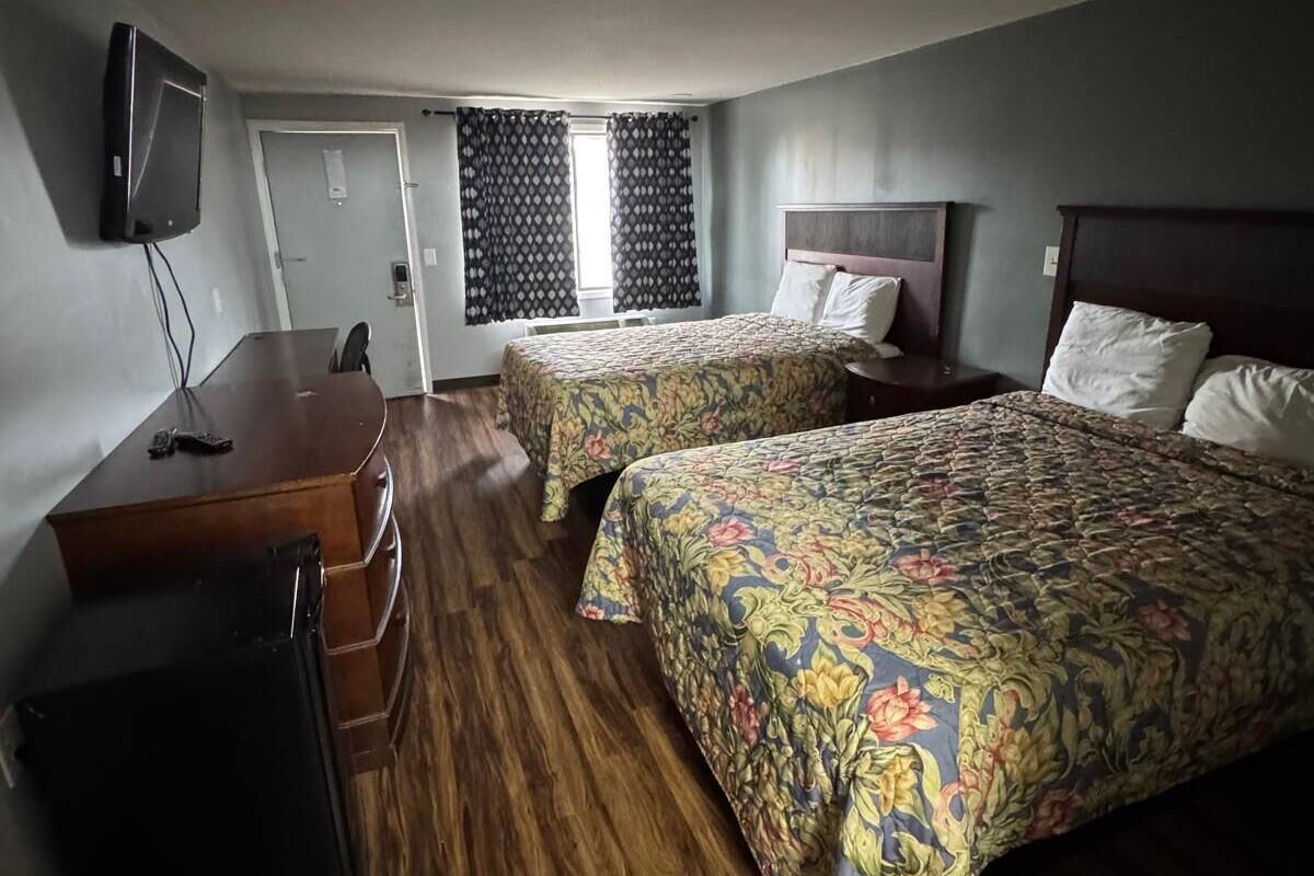 A hotel room with two beds, a desk, a TV, and a window with curtains.