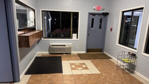 A hotel lobby with a large window, a door with an exit sign, a radiator, and a mat. - Budgetel Inn & Suites (Columbus)