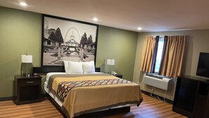 A hotel room with a bed, nightstands, a lamp, a telephone, an air conditioning unit, a television, and a large framed picture on the wall. - Super 8 by Wyndham Joplin (Joplin)