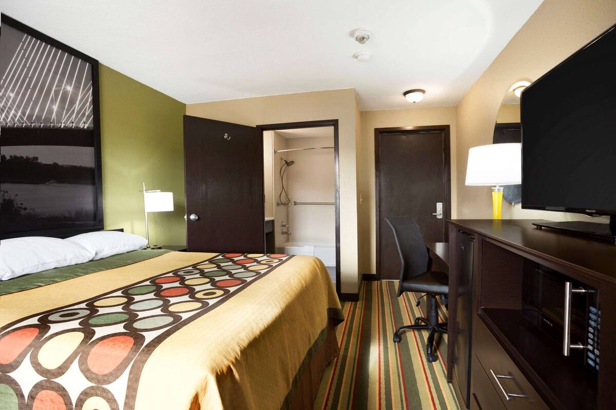 Hotelkamer met een bed, bureau met televisie, douche en deur naar een badkamer.