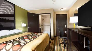 Une chambre d’hôtel comprenant un lit, un bureau avec une télévision, une douche et une porte donnant accès à une salle de bain.