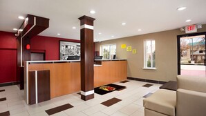 A hotel reception area with a wooden reception desk, a red wall, and a beige couch. - Super 8 by Wyndham Joplin (Joplin)