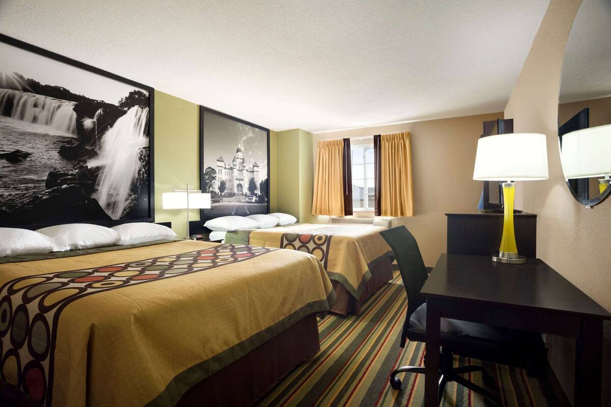 Een hotelkamer met twee bedden, een bureau, een stoel, een lamp en een groot schilderij aan de muur.
