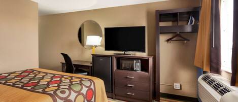 A hotel room with a bed, a desk with a flat-screen TV, a mini-fridge, a microwave, a heater, and a hanging coat rack.