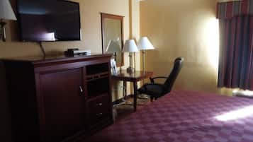 A hotel room with a bed, a desk with two lamps, a television on the wall, and a chair.