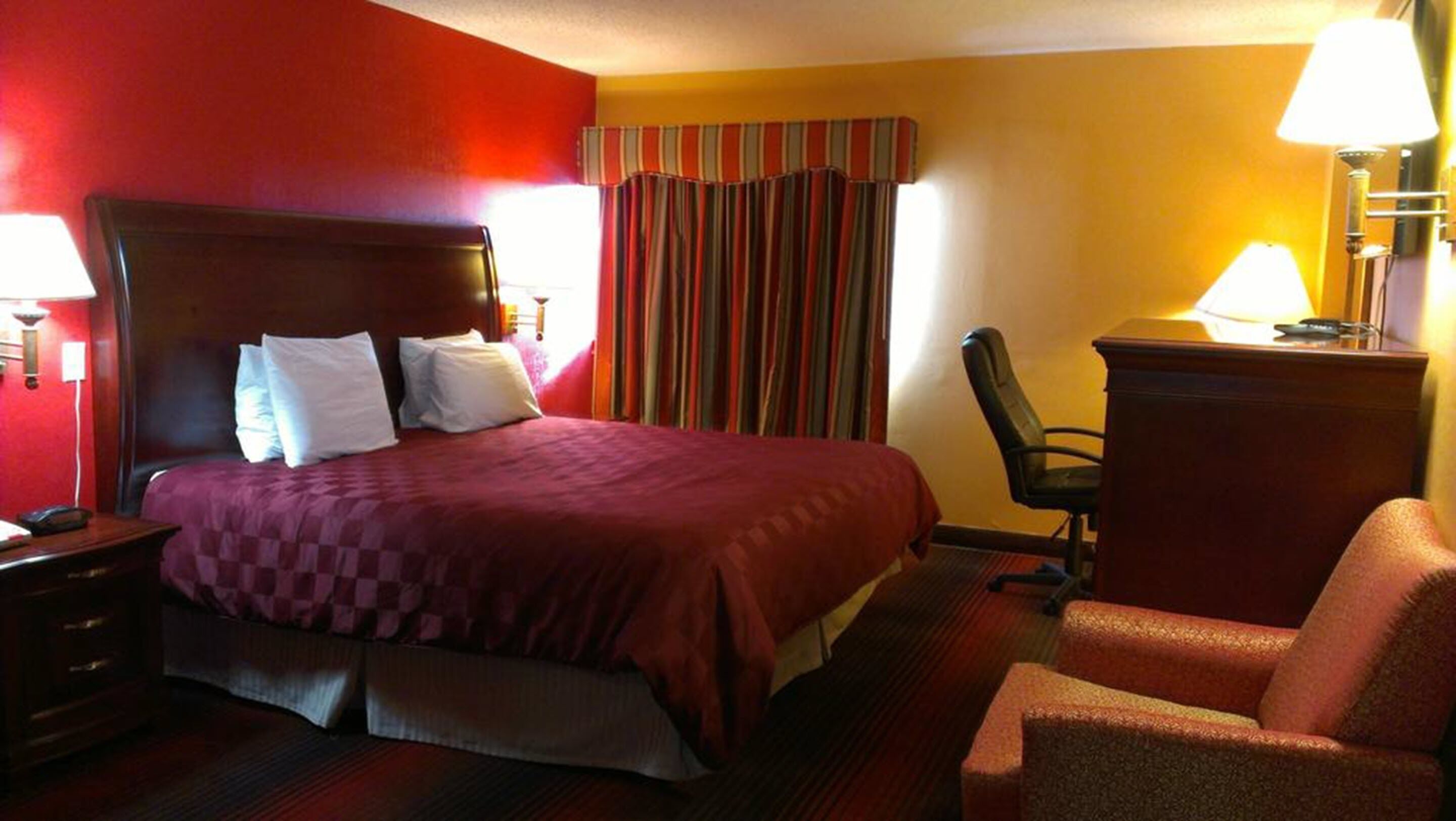 Una habitación de hotel con una cama grande, un escritorio, una silla y una lámpara.