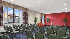 A conference room with rows of green chairs, a red accent wall, and large windows with curtains. - Ramada by Wyndham East Orange (East Orange)