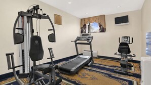 A hotel room with a treadmill, a weight machine, a water dispenser, and a TV on the wall. - Ramada by Wyndham East Orange (East Orange)