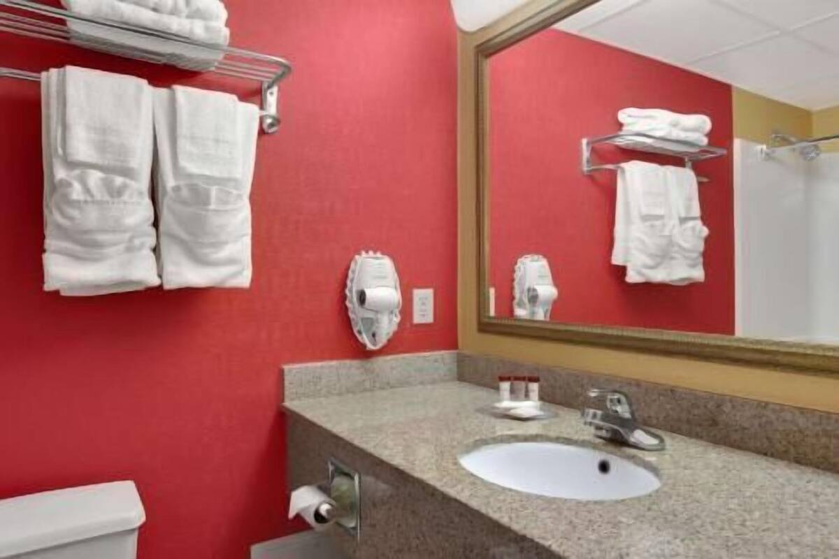 A bathroom with a red wall, a sink, a mirror, and a towel rack.