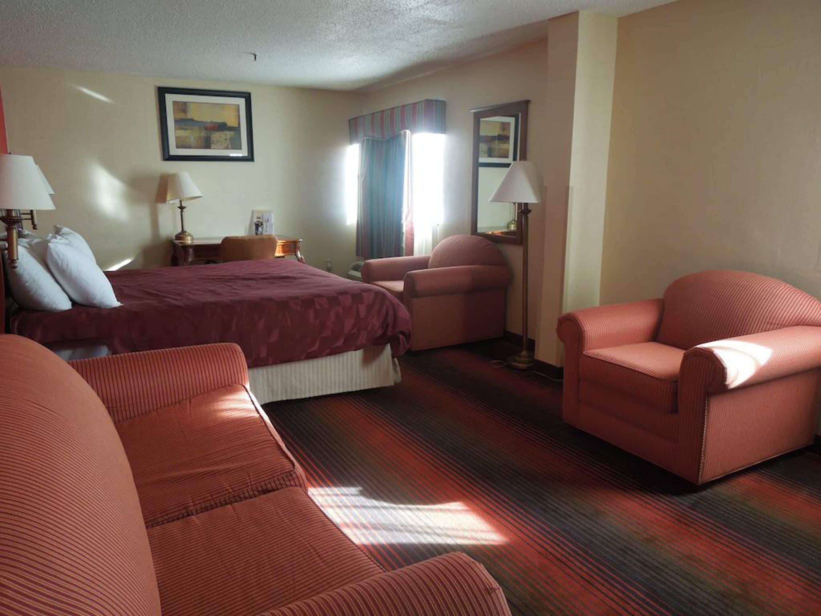Een hotelkamer met een groot bed, twee fauteuils, een bureau en een nachtkastje.