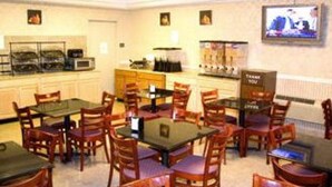 A dining area with multiple tables and chairs, a coffee station, and a television mounted on the wall. - Ramada by Wyndham East Orange (East Orange)