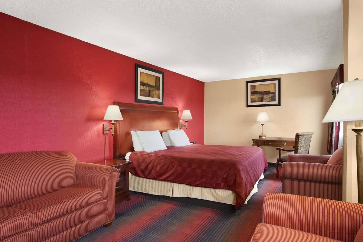 A hotel room with a large bed, two bedside tables with lamps, a desk with a chair, and two armchairs.