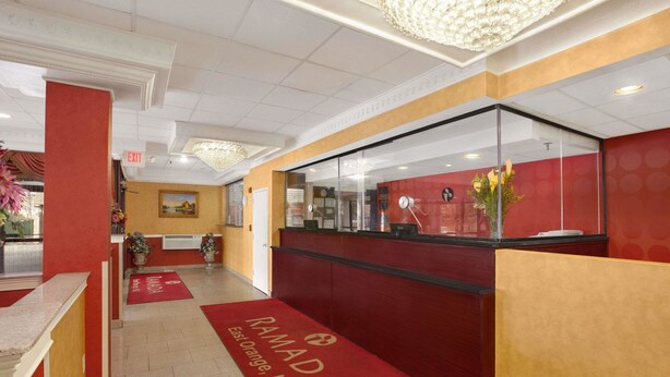 A reception area with a red carpet, a reception desk, and a wall-mounted telephone. - Ramada by Wyndham East Orange (East Orange)