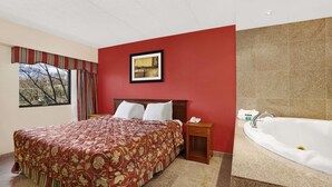 A hotel room with a large bed, a bedside table with a phone, a framed picture on the wall, and a bathroom with a bathtub. - Ramada by Wyndham East Orange (East Orange)