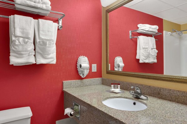 A bathroom with a red wall, a white sink, a mirror, and towels on a rack. - Ramada by Wyndham East Orange (East Orange)