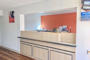 Una zona de recepción con mostrador de madera, una computadora y un tablón de anuncios.