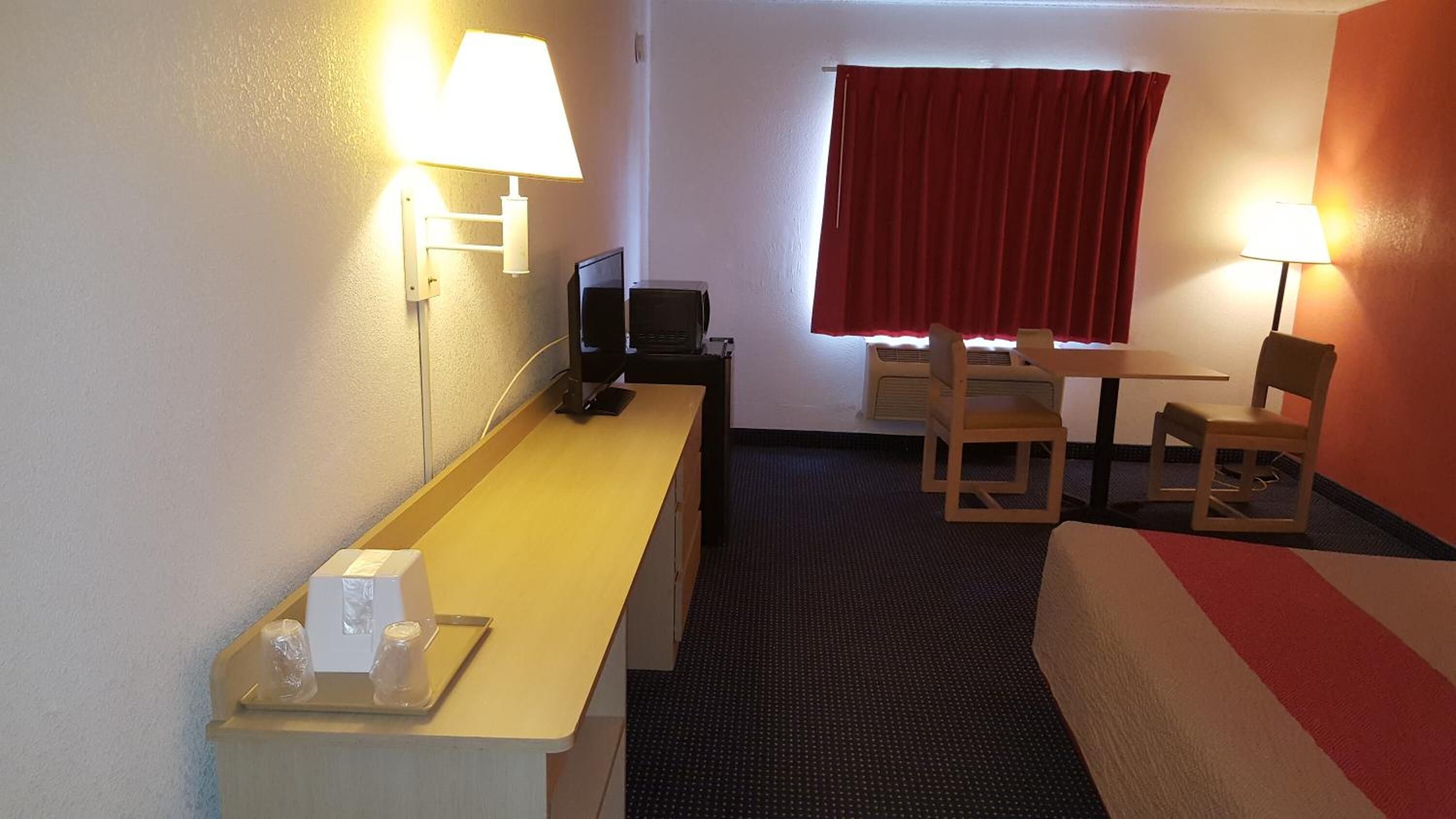 A hotel room with a bed, a desk with a computer, a chair, a table, and two lamps.