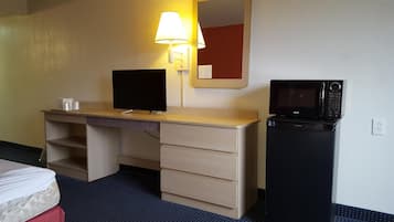 A hotel room with a bed, a desk with a computer monitor, a microwave, and a lamp.
