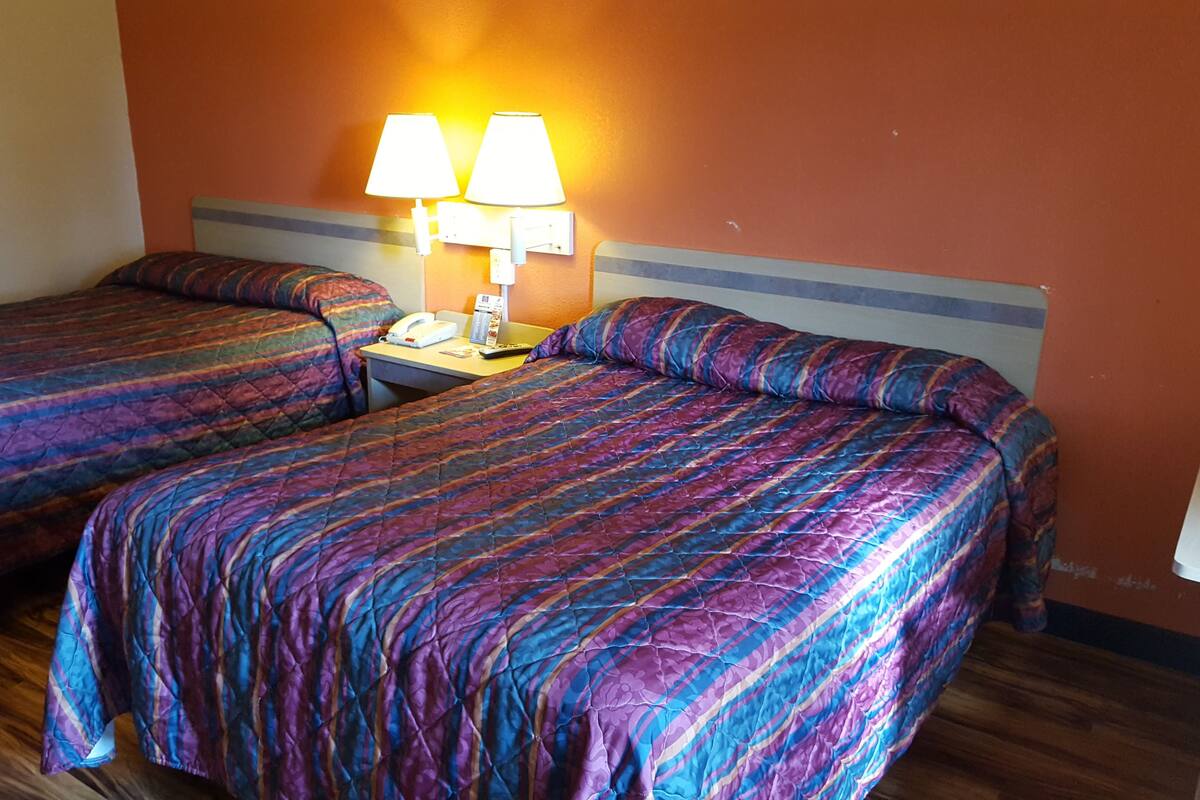Quarto de hotel com duas camas, cada uma com colcha listrada, mesa de cabeceira com abajur e telefone.