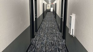 A long, narrow hotel corridor with doors on both sides, a patterned carpet, and a ceiling light. - Super 8 Springfield North I-44 (Springfield)