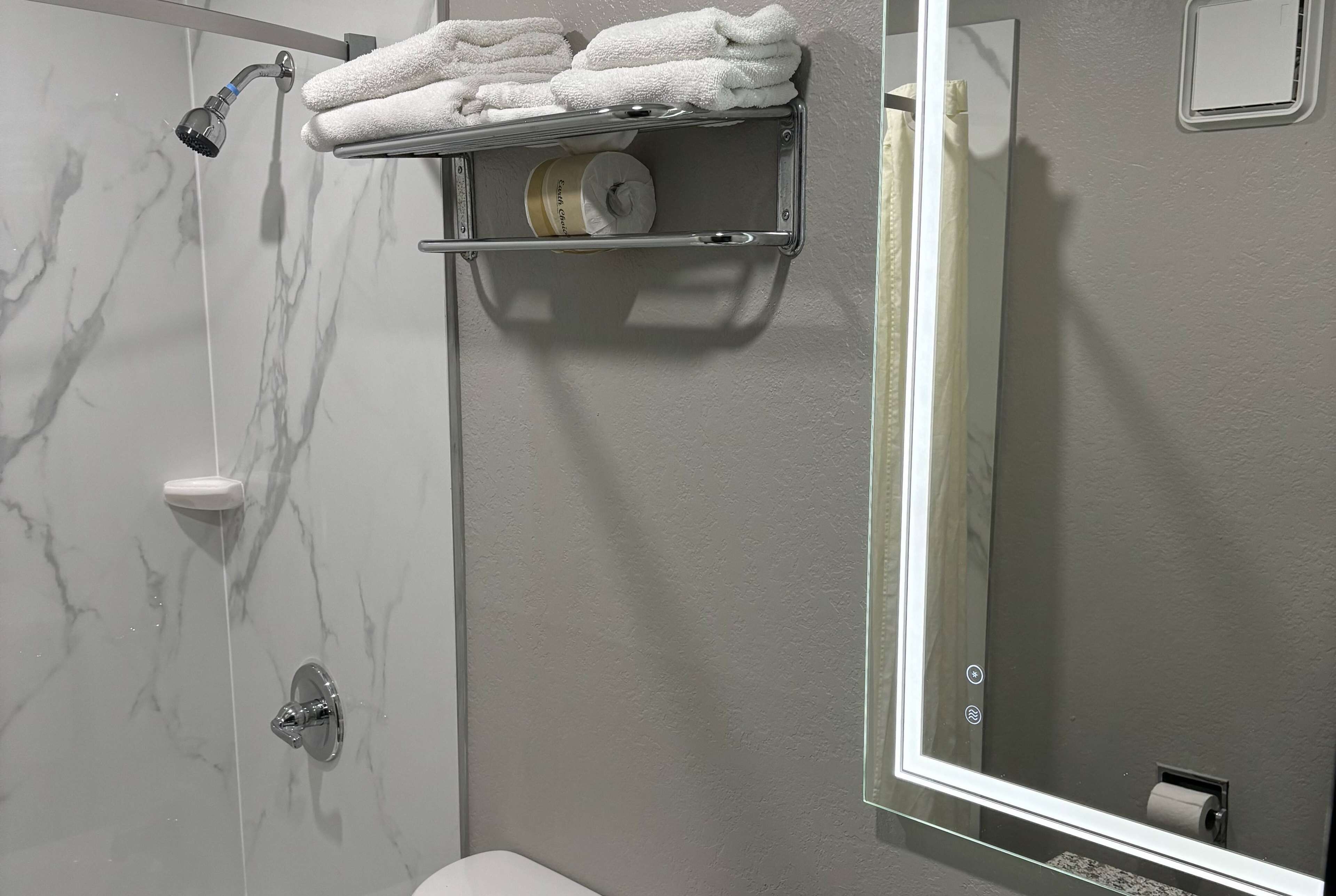 A bathroom with a marble wall, a shower, a toilet, a towel rack with towels, and a toilet paper holder.