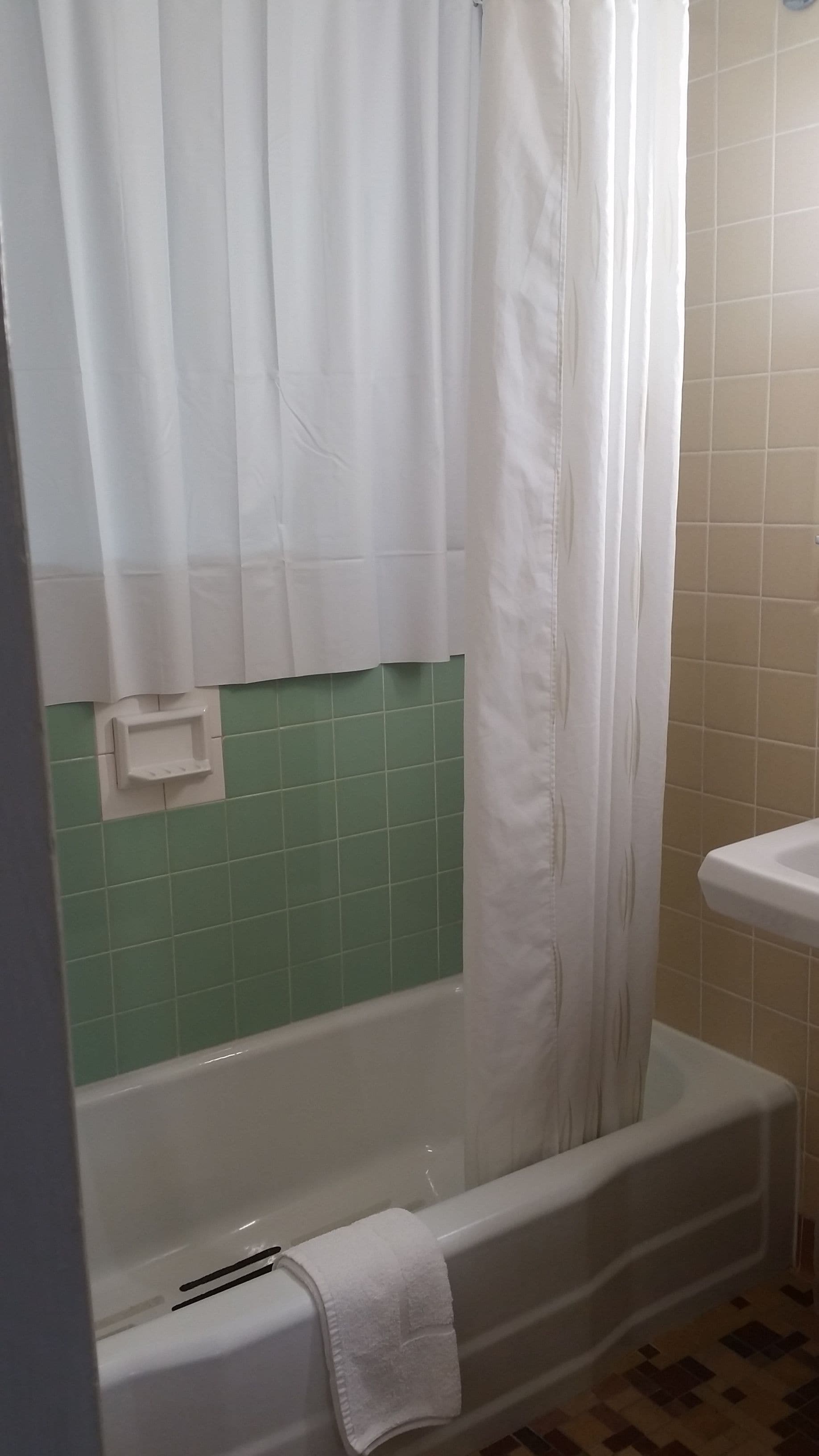 Un baño con bañera, cortina de ducha blanca y paredes con azulejos verdes.
