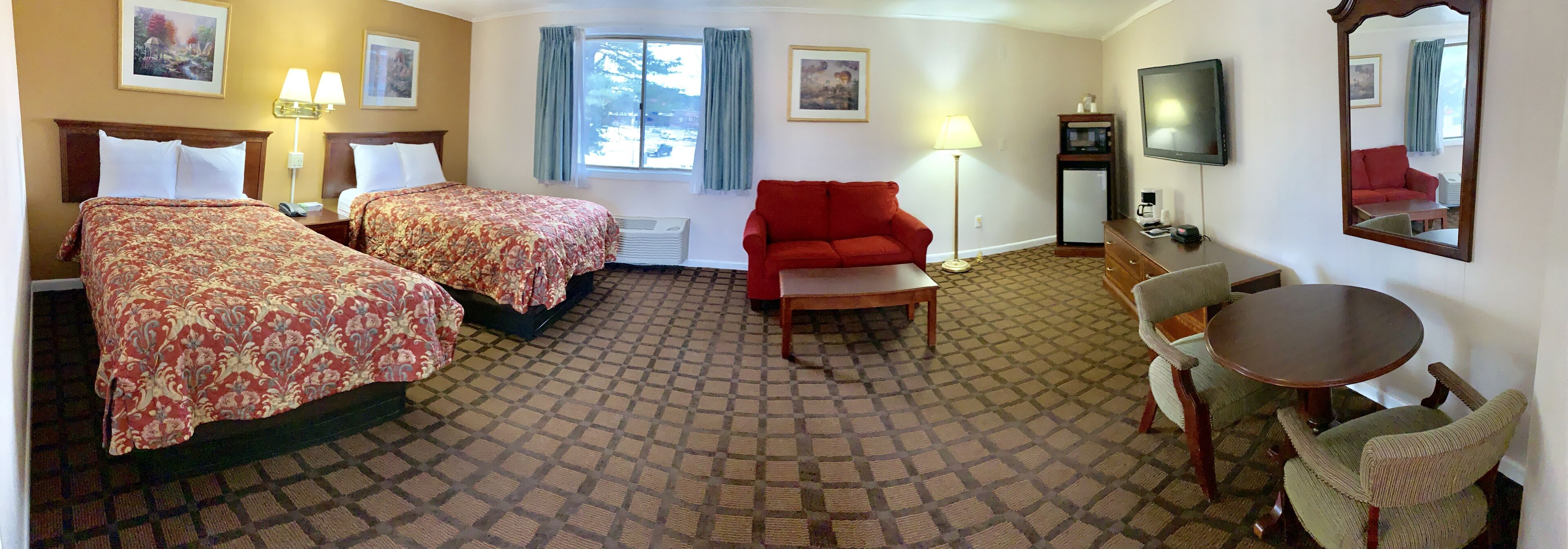 Une chambre d’hôtel avec deux lits, un canapé rouge, une table ronde, une télévision et un miroir.