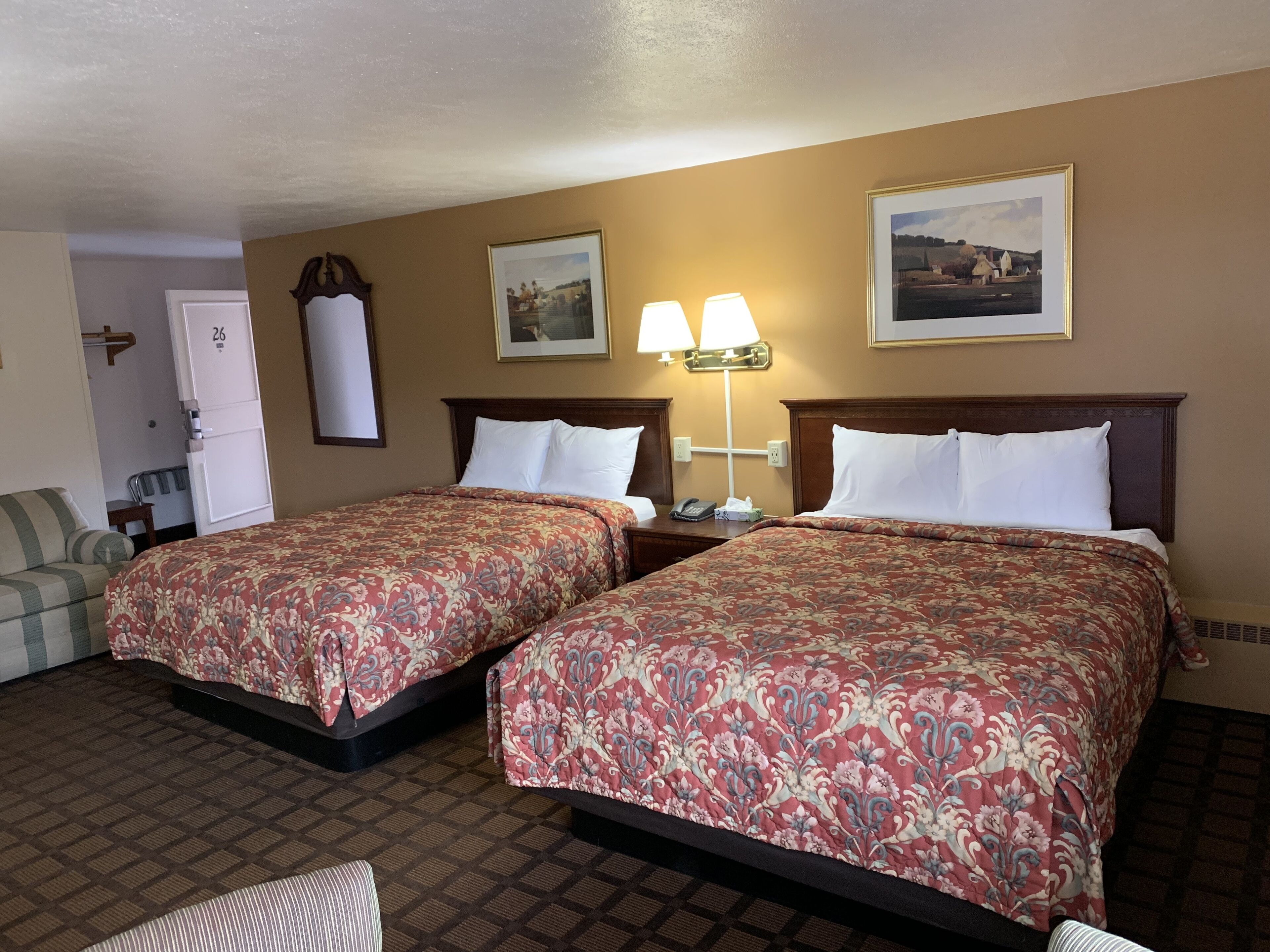 A hotel room with two beds, a sofa, a desk, a phone, and two wall-mounted lamps.