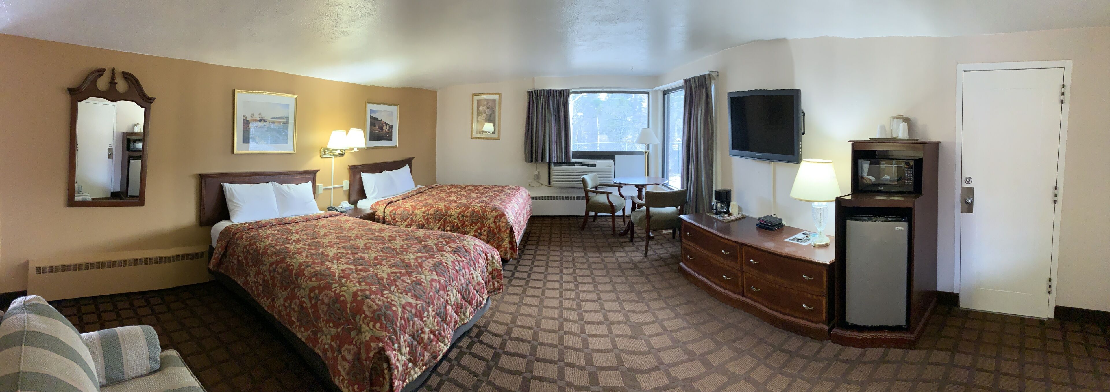Ein Hotelzimmer mit zwei Betten, einem Schreibtisch, einem Fernseher, einer Mikrowelle und einem Fenster mit Vorhängen.