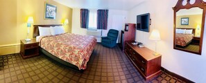 A hotel room with a bed, a desk, a chair, a TV, and a mirror.