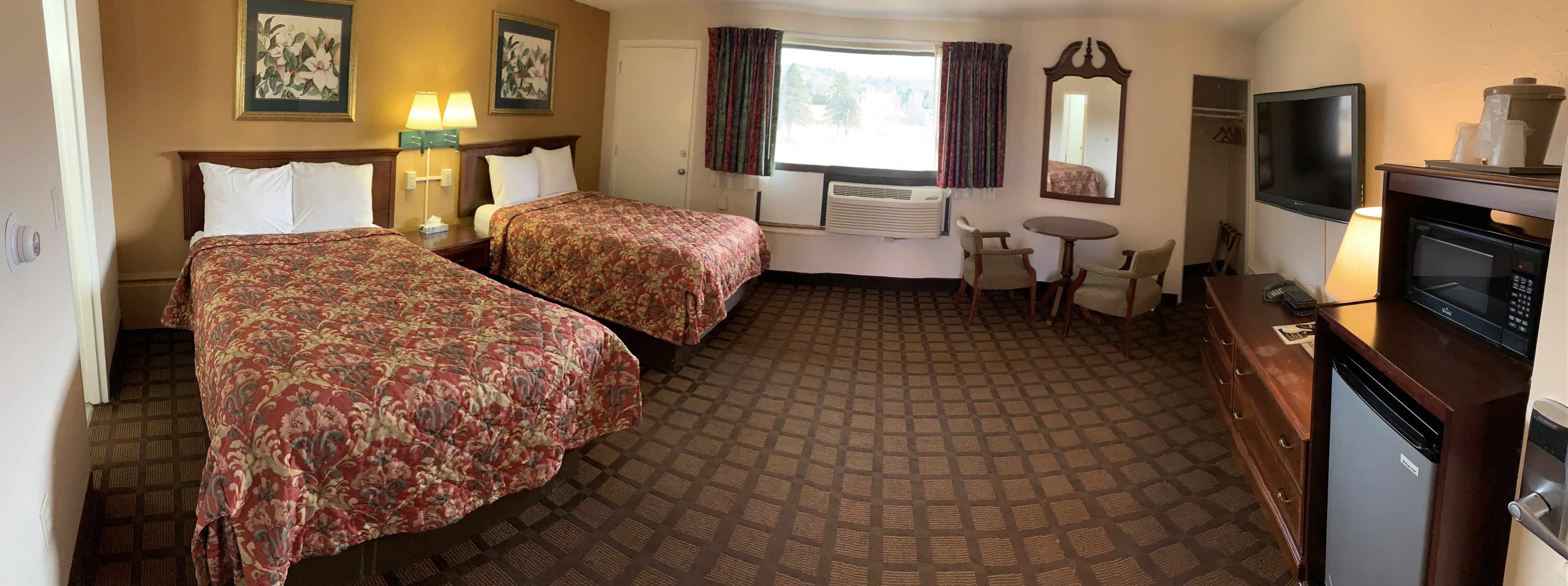 A hotel room with two beds, a small table with chairs, a television, a microwave, and a refrigerator.