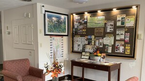 A lobby with two red patterned armchairs, a wooden coffee table, a bulletin board with various notices, and a framed map on the wall.