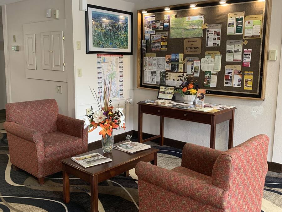 A lobby with two red patterned armchairs, a wooden coffee table, a bulletin board with various notices, and a framed map on the wall.