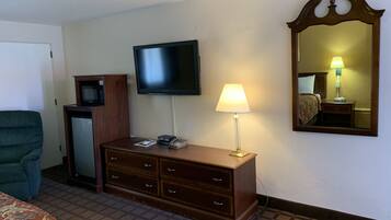 A hotel room with a TV, a bedside lamp, a dresser, a mirror, and a bed.