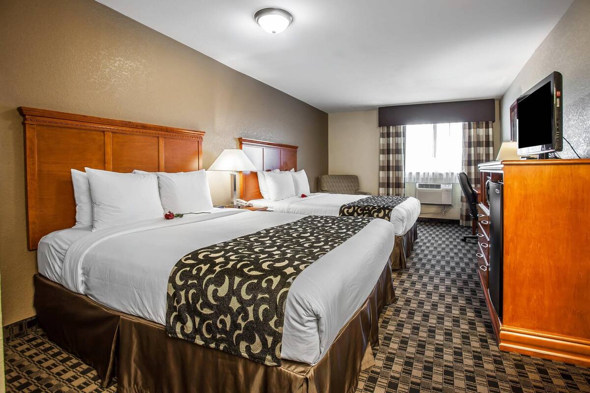 A hotel room with two beds, a desk, a television, and a window with curtains.
