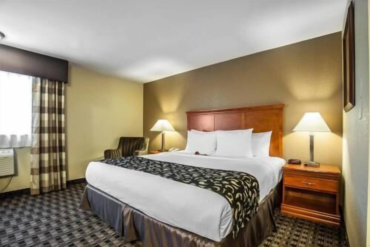 A hotel room with a bed, two bedside tables, a chair, and a window with curtains.