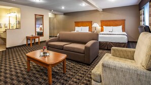 A hotel room with a sofa, armchair, and a bed with a wooden headboard.