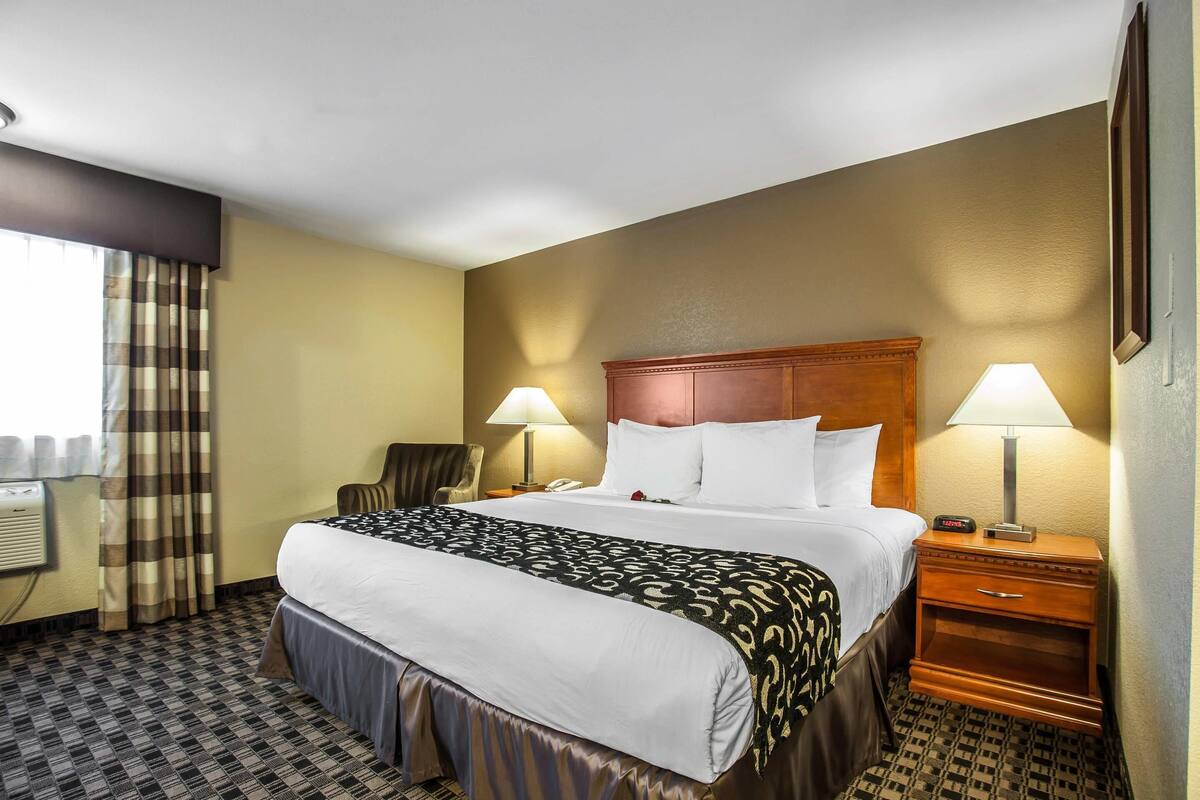 A hotel room with a large bed, two bedside tables with lamps, a chair, and a window with curtains.