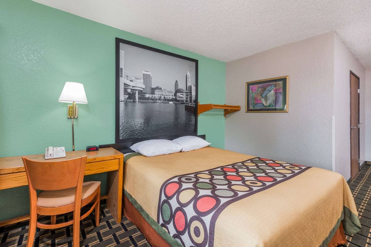 Hotelkamer met een bed, een bureau met stoel, een lamp, een stadsgezicht in een lijst en een schilderij aan de muur.