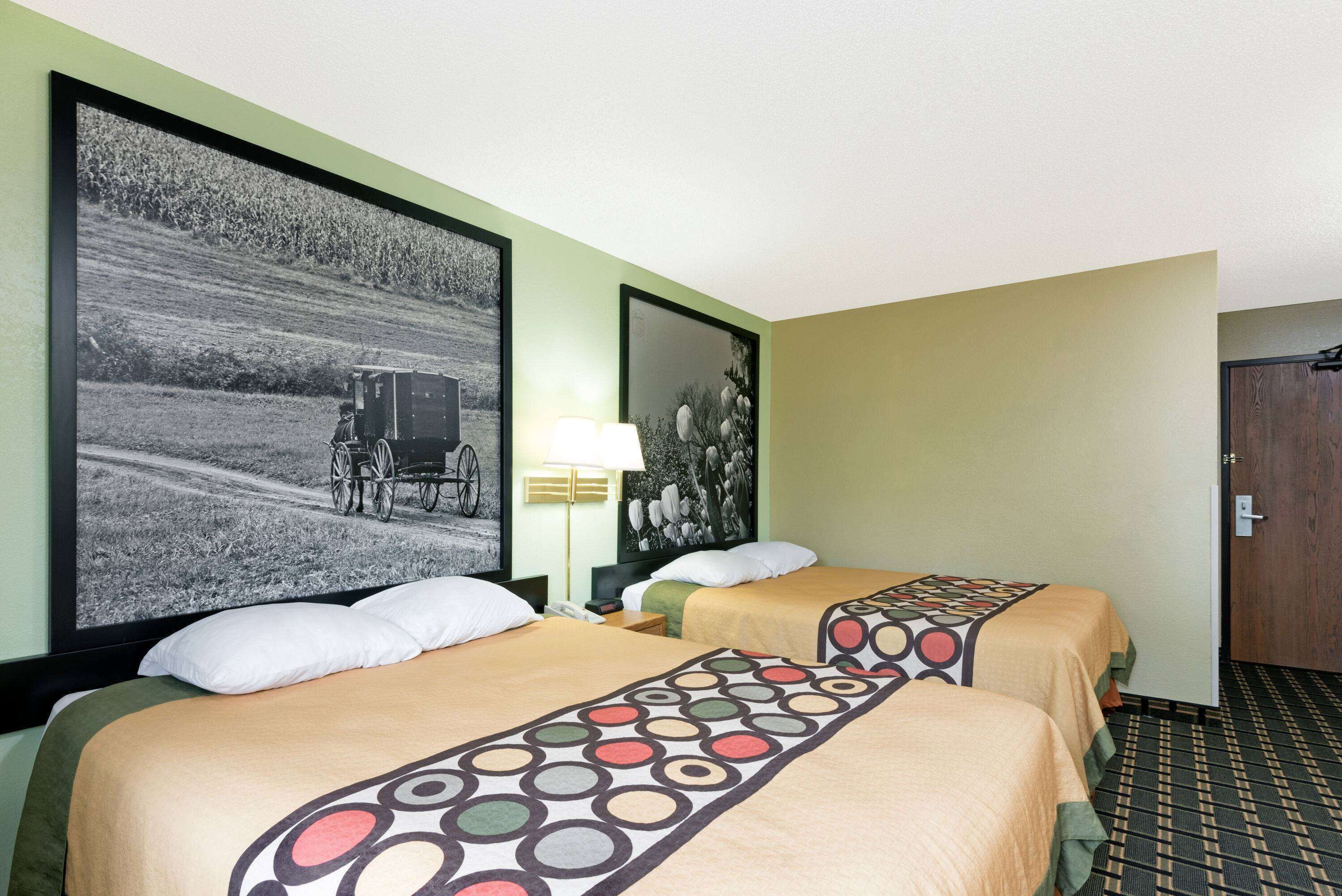 A hotel room with two beds, a large framed picture on the wall, a lamp, and a door.