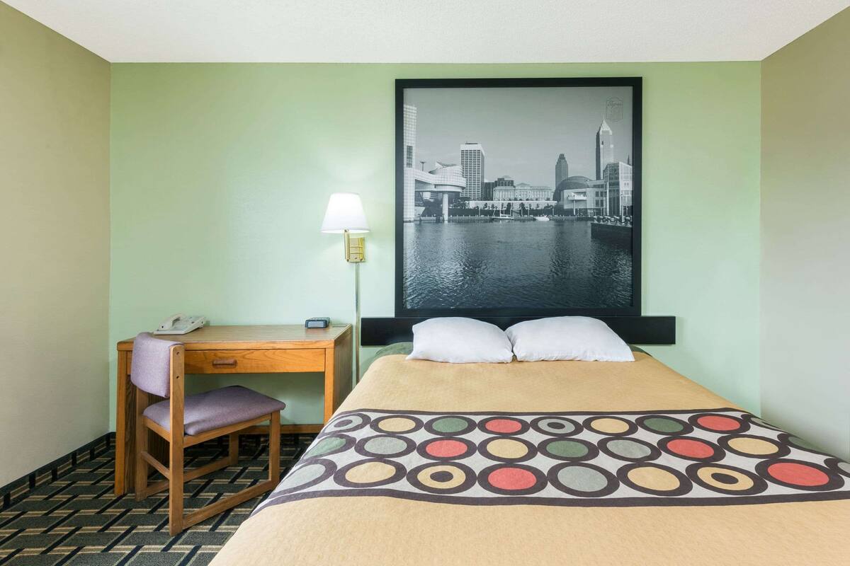 Een hotelkamer met een bed, een bureau met stoel, een lamp en een stadsgezicht poster op de muur.
