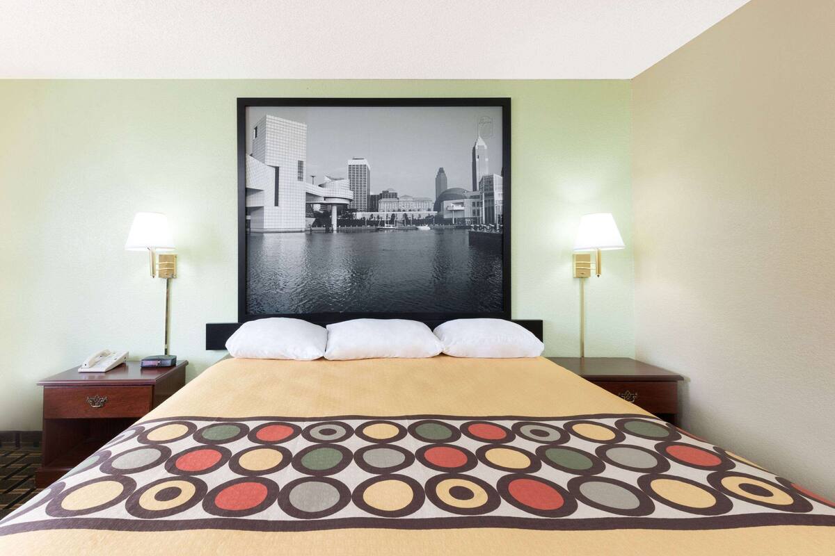 Een hotelkamer met een bed, twee nachtkastjes, een kunstwerk met een stadsgezicht en twee lampen.