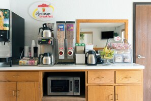 Een kitchenette met een koffieapparaat, een magnetron en diverse etenswaren op het aanrecht.