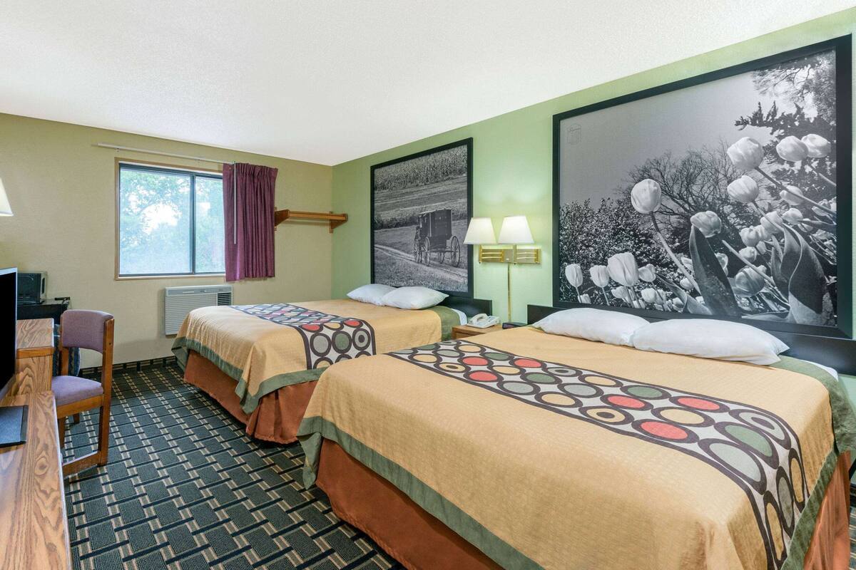 Een hotelkamer met twee bedden, een bureau, een stoel, een raam met gordijnen, een lamp en twee wandlampen.